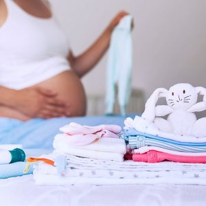Schwangere Frau hinter Wickeltisch mit Babykleidung und einem Plüschtier