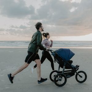 Eltern joggen mit Kinderwagen am Strand.