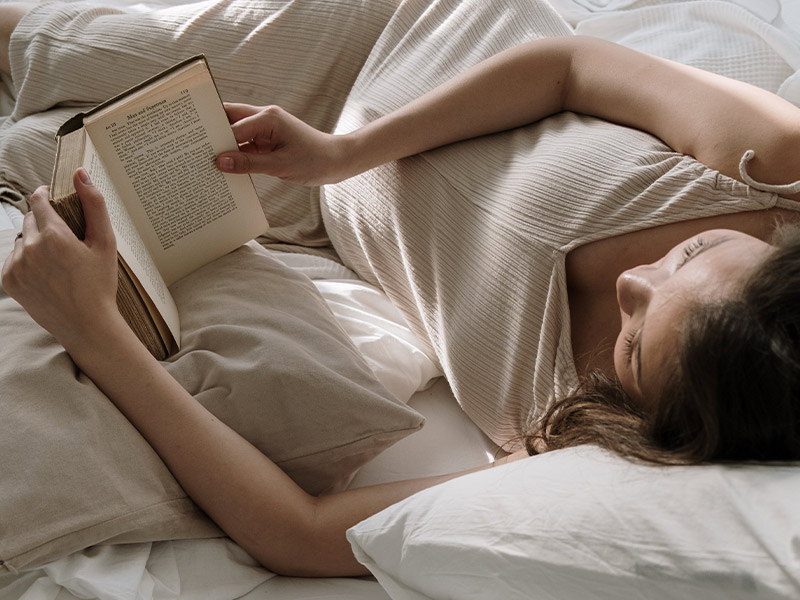 Schwangere Frau liest ein Buch, auf der Seite liegend