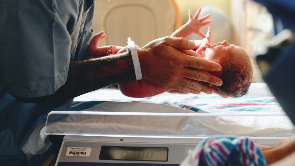 Neugeborenes direkt nach der Geburt bei Messung des Geburtsgewicht von Krankenschwester