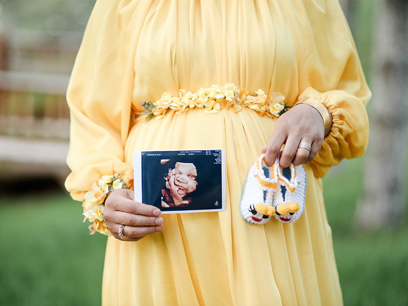 Schwangere Frau mit Ultraschall Bild von zweiter Schwangerschaft und Babyschuhen