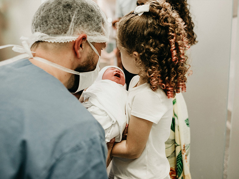 Vater und Tochter halten neugeborenes Baby im Arm nach Entbindung im Geburtsort Klinik