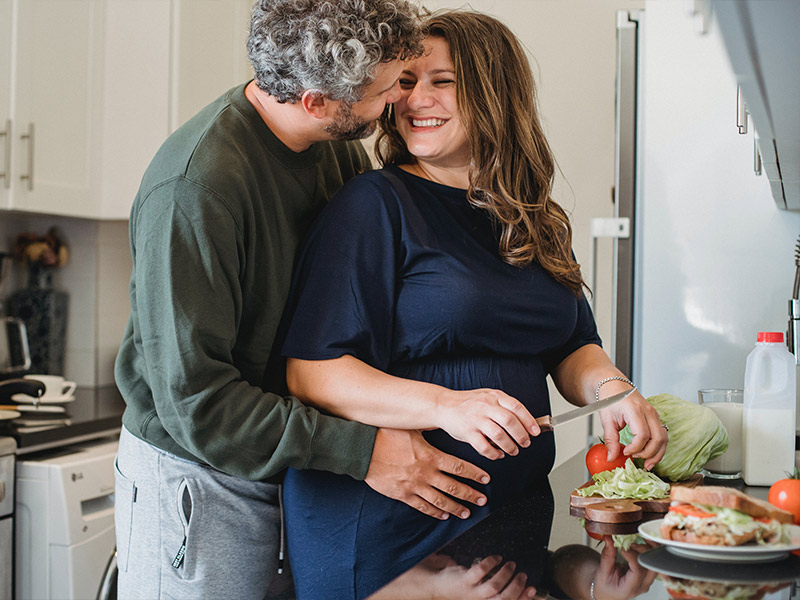 Pärchen mit schwangerer Frau beim Kochen von vegangen Gerichten